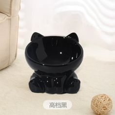 a black cat shaped bowl sitting next to a ball of yarn on the floor in front of a chair