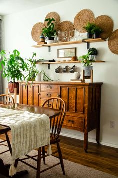 a dining room table and chairs with plants on the shelves above it, in front of a window