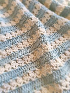 a crocheted blanket is laying on top of a bed with blue and white stripes