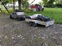 two toy trucks are parked next to each other on the ground near some trees and grass