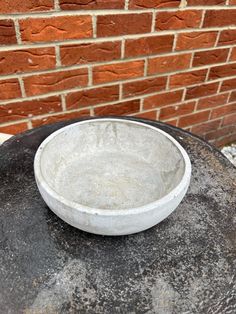 a white bowl sitting on top of a black table next to a brick wall and sidewalk