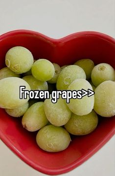 a red bowl filled with green grapes in the shape of a heart on top of a white table