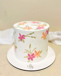 a white cake with pink and orange flowers on it sitting on a plate next to a napkin