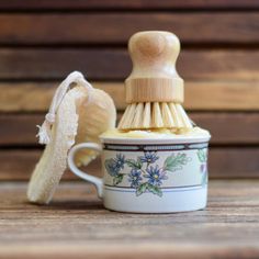 a cup with a brush inside on a wooden table next to a piece of bread