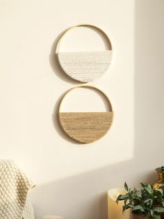 two circular wall hangings on the side of a white wall next to a potted plant