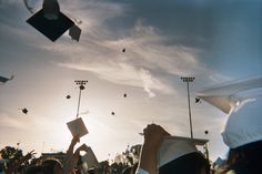 graduates throwing their caps in the air at graduation ceremony with sun shining behind them and flying high above