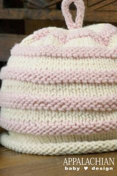 a pink and white knitted hat sitting on top of a wooden table