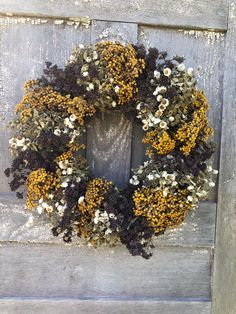 a wreath with yellow and white flowers hanging on a wooden door frame in front of a weathered wall