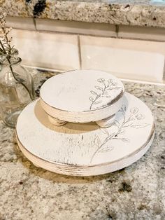 three plates sitting on top of a counter next to a vase with flowers in it