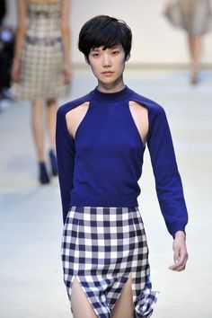 a model walks down the runway in a blue top and plaid skirt