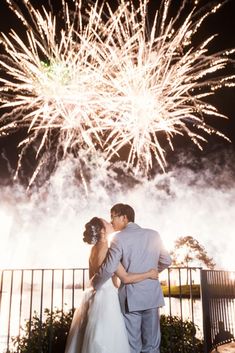 a bride and groom kissing in front of fireworks