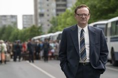 a man in a suit and tie standing on the side of a road with people behind him