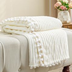 a white blanket with pom - poms sitting on top of a bed next to a vase