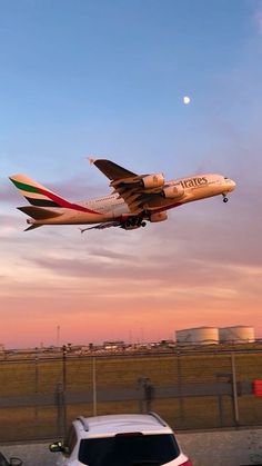 an airplane taking off from the runway at sunset or dawn with cars parked in front of it