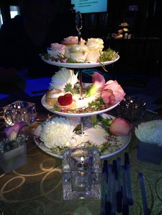 three tiered trays with cupcakes and flowers on them at a party