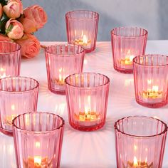 many pink glass cups with candles in them on a white table cloth next to flowers