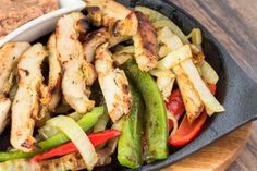 a skillet filled with chicken and vegetables on top of a wooden cutting board next to a bowl of dipping sauce