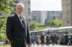 an older man in a suit and tie standing on the street with people walking by