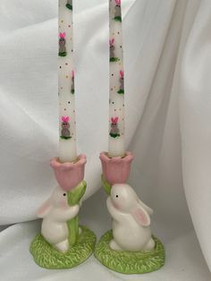 two white candles with pink and green flowers on them sitting next to each other in front of a white background