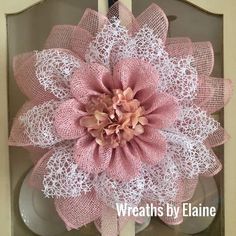 a pink and white flower is on display in a glass case with lace around it