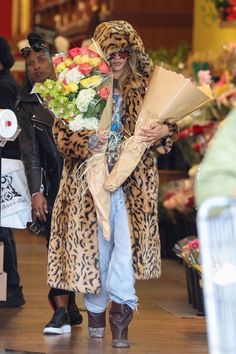 a woman in leopard print coat holding flowers while walking down the street with other people