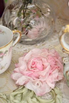 a pink rose sitting on top of a table next to tea cups and saucers