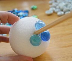 a hand holding a wooden stick over a white ball with blue and green candies on it