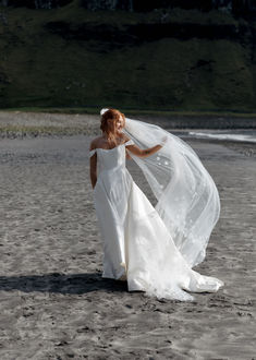 a woman in a wedding dress on the beach with her veil blowing in the wind