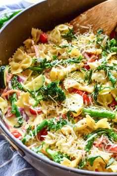 a pan filled with pasta and vegetables on top of a blue towel next to a wooden spoon