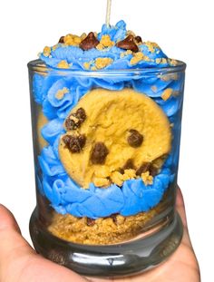 a cookie in a jar with blue icing and chocolate chips on top, being held by a person