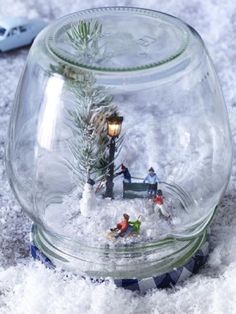 a glass jar filled with miniature figurines on top of snow