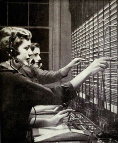 two women in headphones are working on some type of computer equipment that is lined up against the wall