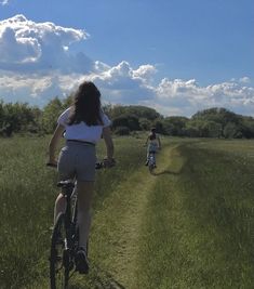 two people riding bikes on a dirt path in the middle of an open field with tall grass