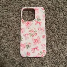 an iphone case with pink bows on it sitting on a carpeted floor next to a cell phone