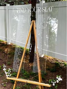 a wooden easel stands in front of a tree with the words find your seat written on it