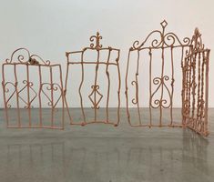 three wrought iron gates sitting next to each other on a cement floor in front of a white wall