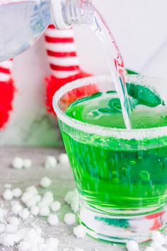 a person pouring water into a cup filled with green and red jellos on top of snow