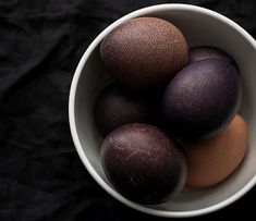 three eggs in a white bowl on a black background with one brown and one dark colored egg