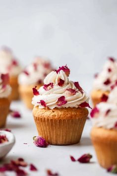 several cupcakes with white frosting and rose petals