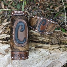 two brown and black leather cuff bracelets on top of a tree stump in the woods