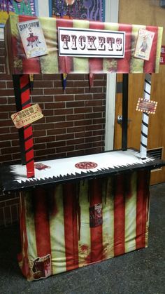 a carnival ticket booth sitting in front of a brick wall with red and white striped curtains