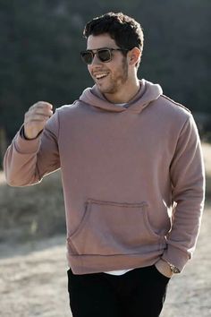 a man wearing sunglasses and a hoodie is walking in the sand with his hand up