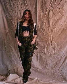 a woman standing in front of a white backdrop wearing camo pants and a black crop top