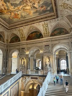 people are walking up and down the stairs in an ornately decorated building with paintings on the ceiling