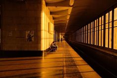 people are sitting on benches in an empty subway station at night with the sun shining through the windows