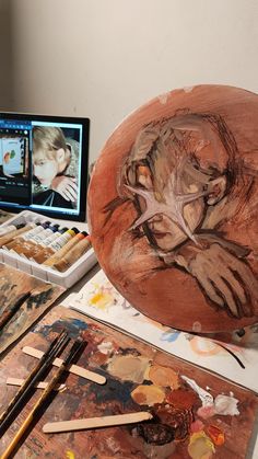 a wooden bowl sitting on top of a table next to a laptop computer and painting supplies