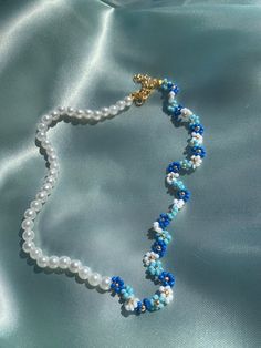 a blue and white beaded necklace is laying on a satin material surface, with a gold - plated charm