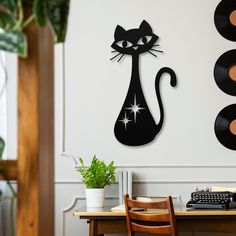 a black cat sitting on top of a wooden table next to record records and a plant