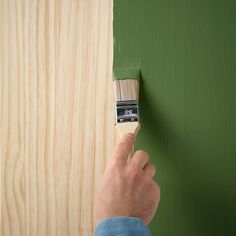 a person holding a paintbrush on top of a green painted wood paneled wall