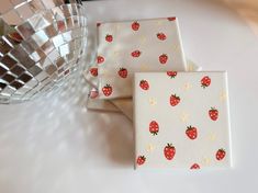 three napkins with strawberries on them are next to a glass bowl and vase